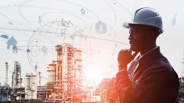 Male industrial engineer wearing a hard hat in a business suit with a manufacturing facility in the background. Abstract concept of technology and cybersecurity overlay.
