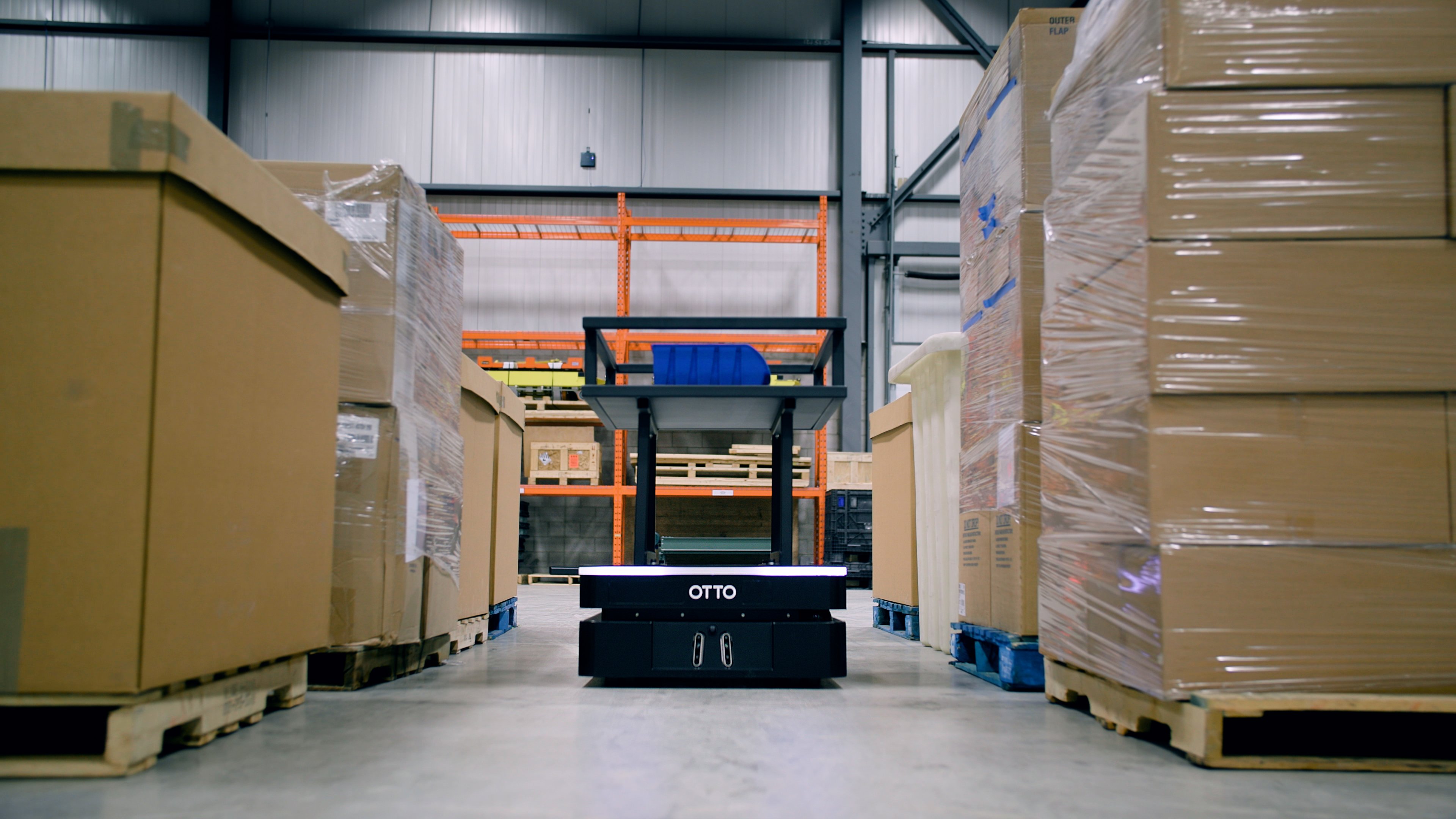 An autonomous mobile robot vehicle, the OTTO 600 AMR robot, moves through a tight warehouse aisle, designed for warehouse logistics and material handling
