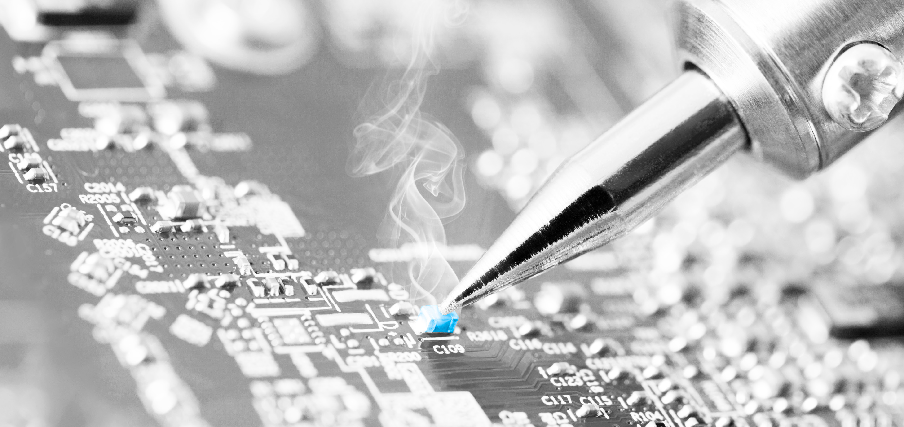Black and white close-up photo of a soldering iron tip working on an electronics circuit board