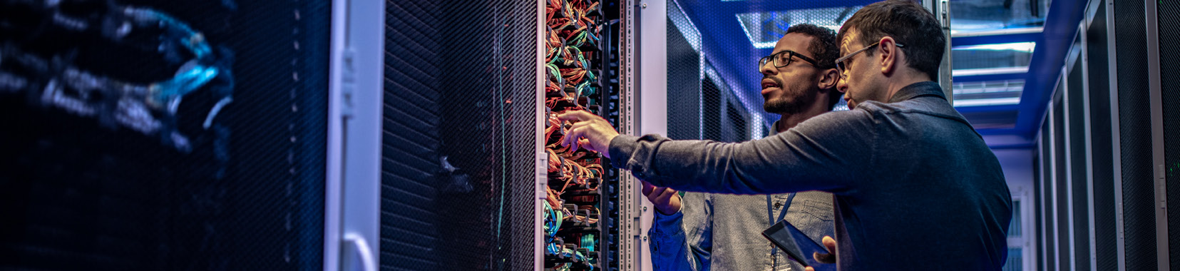 Two workers inspecting server racks in a data center with blue lighting