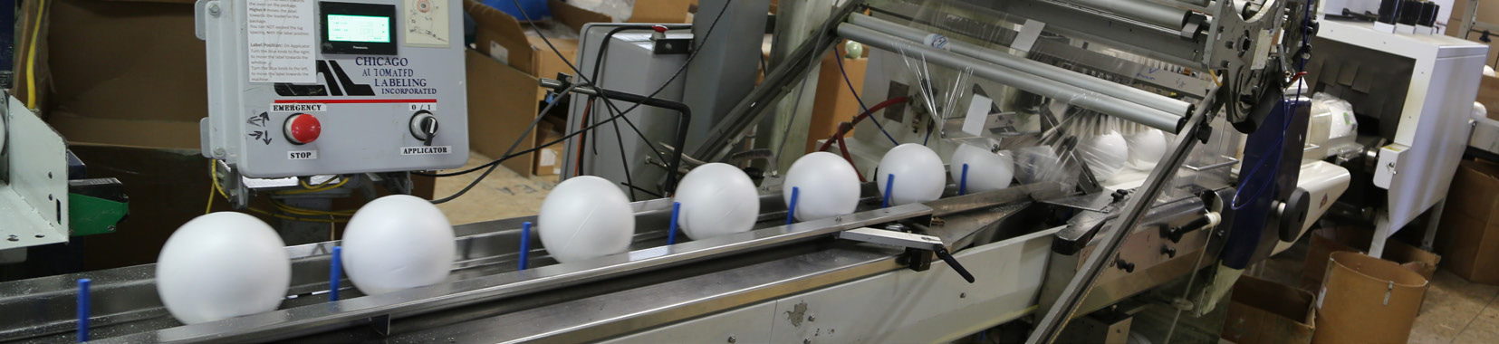 manufacturing facility interior photo with white spherical objects on a conveyor belt and machinery in the background