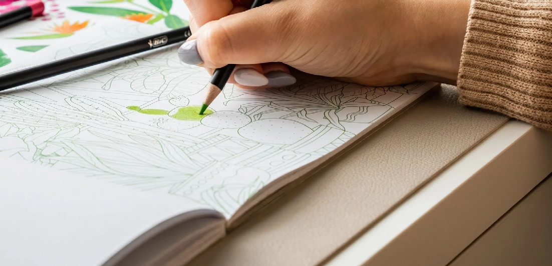 hand coloring a detailed drawing on a white sheet with colored pencils, close-up photo