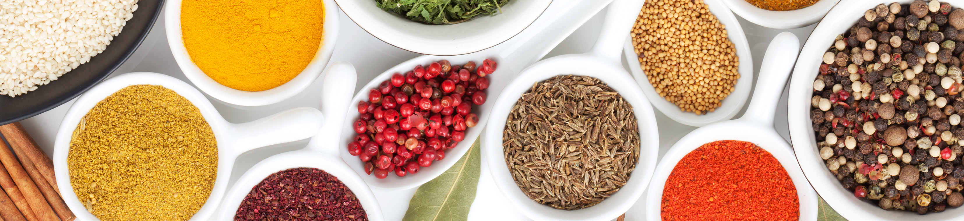 close-up photo of various spices and herbs in round containers on a white surface