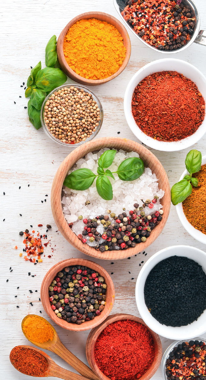top-down view of various spices and herbs in wooden bowls and spoons on white background