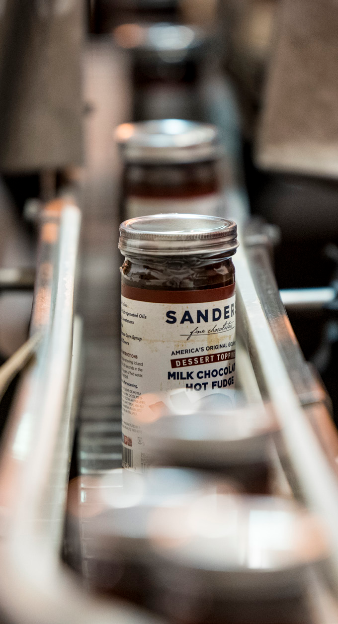 Glass jars of Sanders milk chocolate hot fudge on a production line in a factory