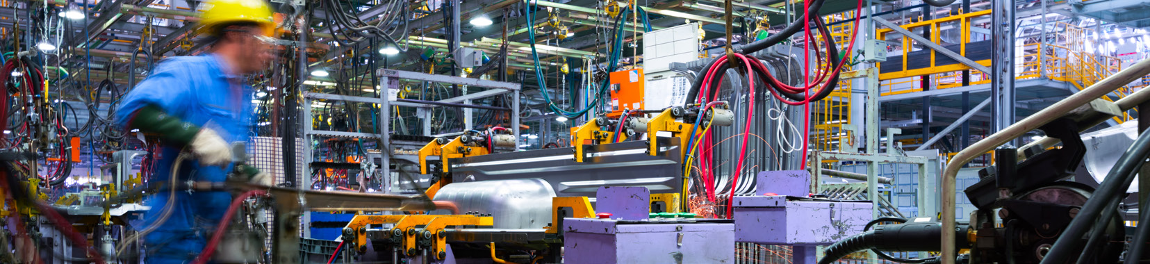 manufacturing facility interior with worker in blue uniform and yellow helmet operating machinery