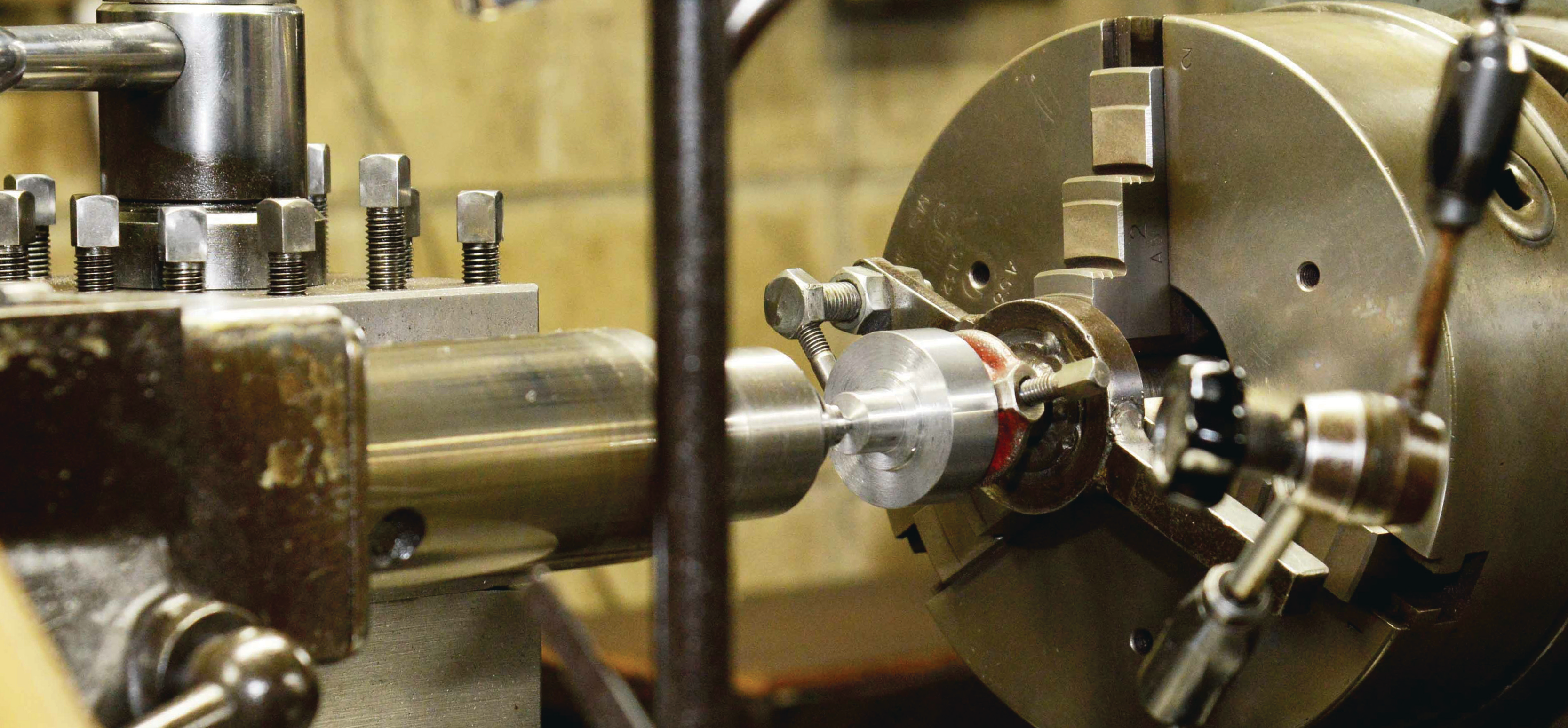 close-up photo of a metal lathe machine chuck holding a cylindrical metal part in a manufacturing facility