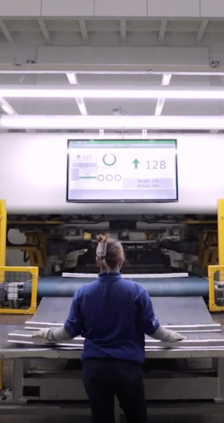 Manufacturing facility interior photo showing a worker standing at a control panel with overhead lighting