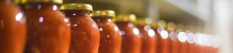 Row of glass jars filled with red sauce in a production line, factory interior photo