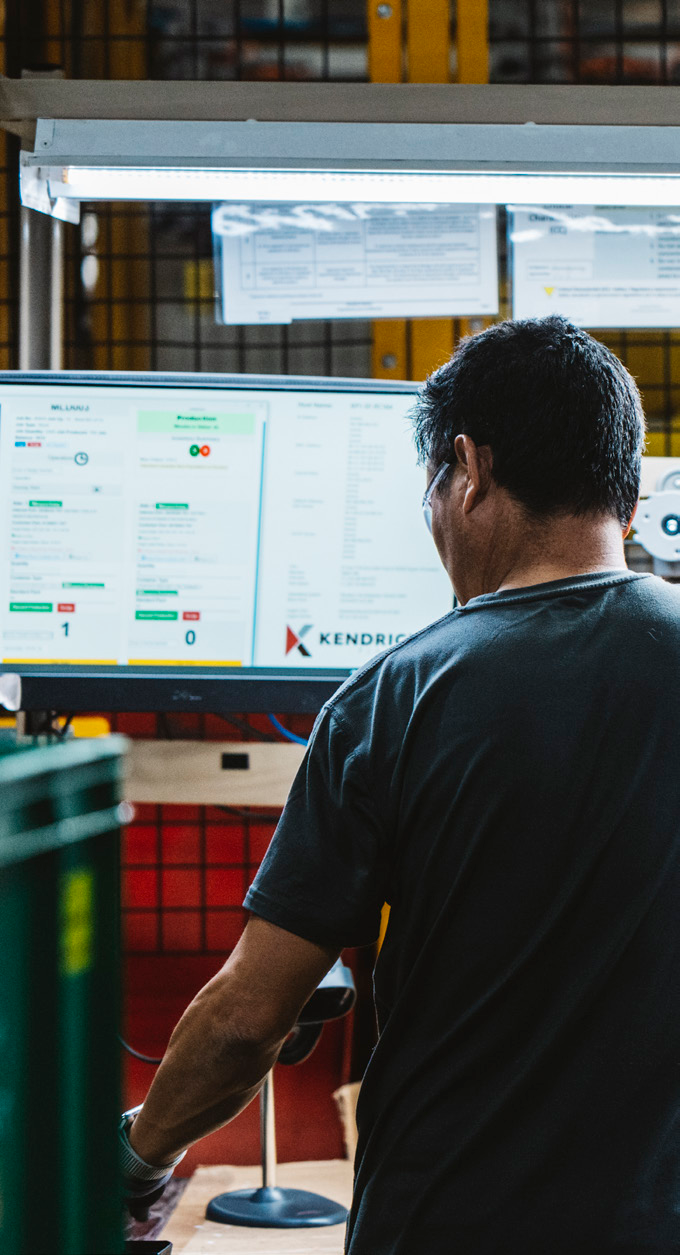 Man operating production line in a manufacturing facility with computer screens in the background