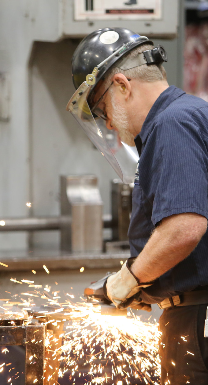 Worker operating a grinding tool with sparks flying in a manufacturing facility