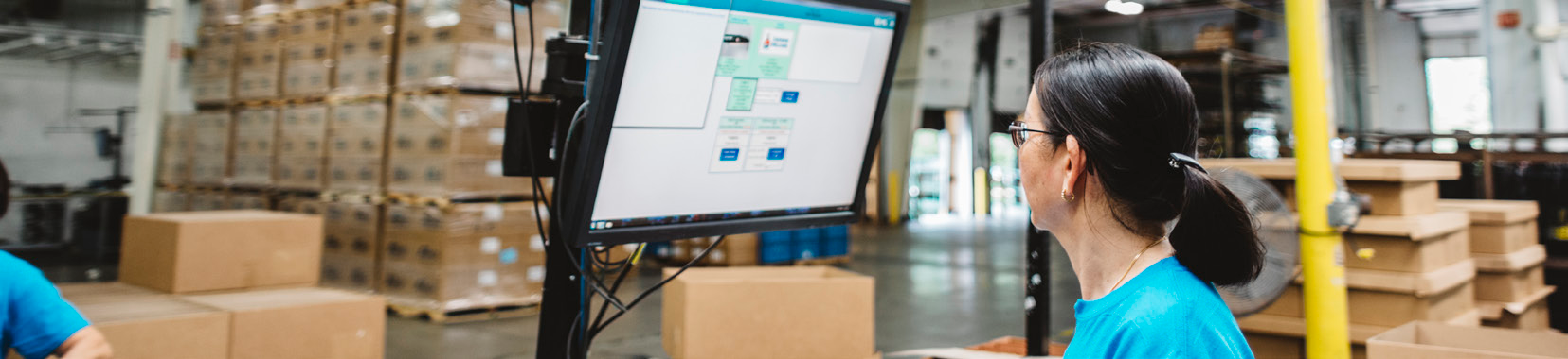 manufacturing facility interior with worker monitoring a screen and stacked boxes in the background
