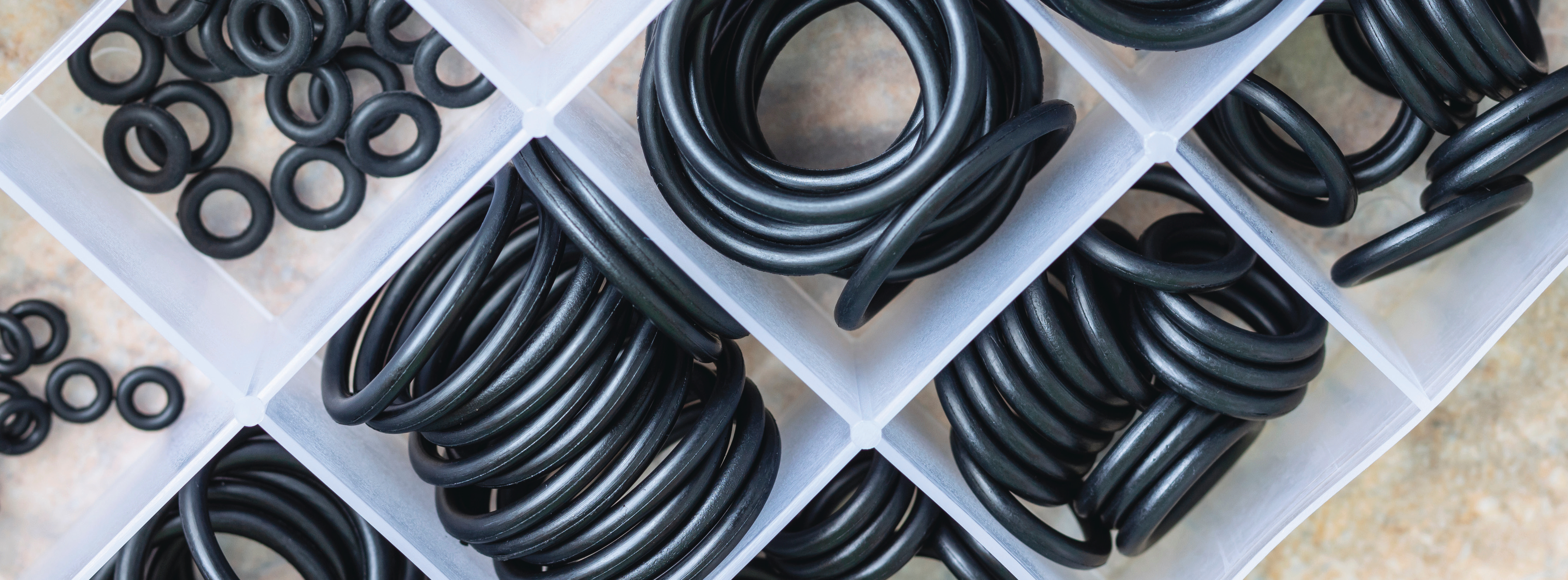 close-up photo of black rubber O-rings and coiled tubing arranged in white trays on a beige surface