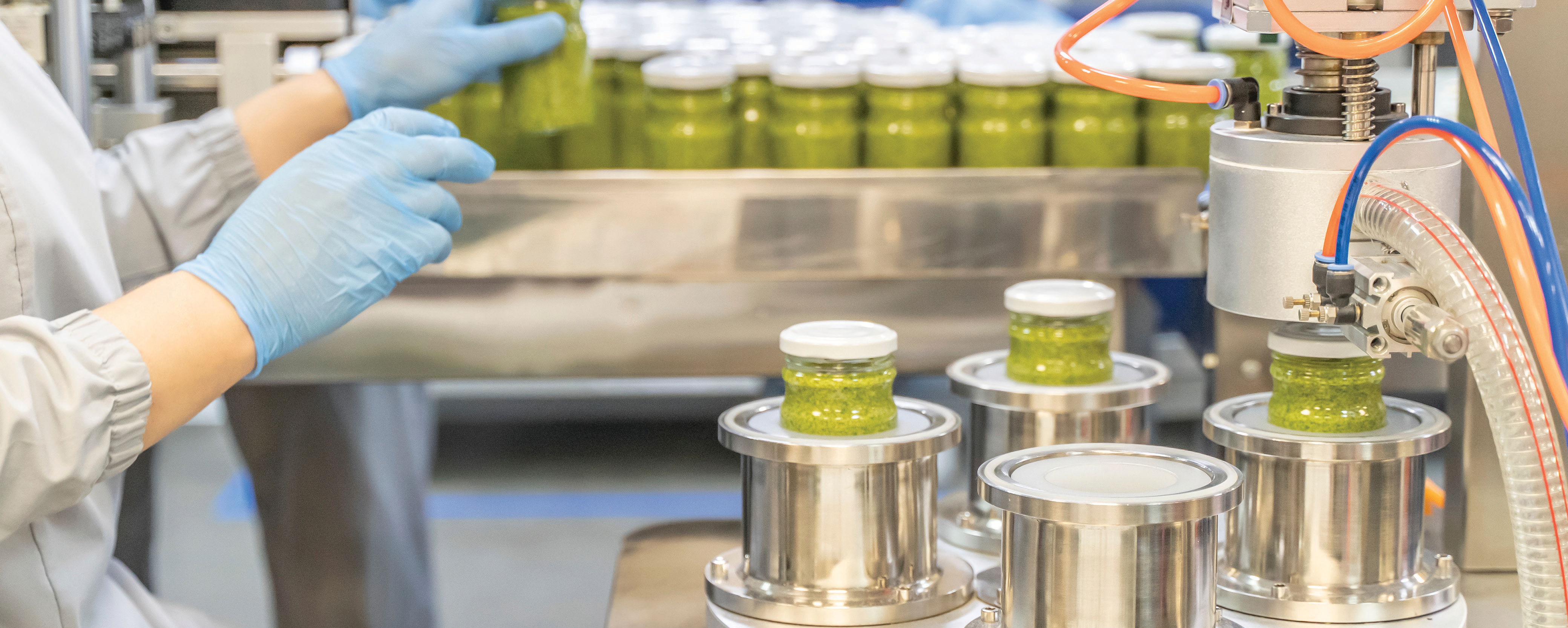 worker operating production line in a manufacturing facility with green jars on conveyor