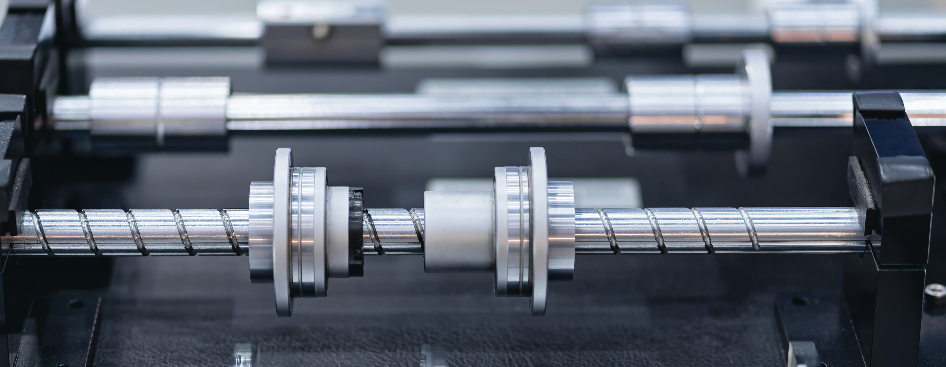 close-up photo of a metal mechanical component with threaded rods and bearings in a factory setting