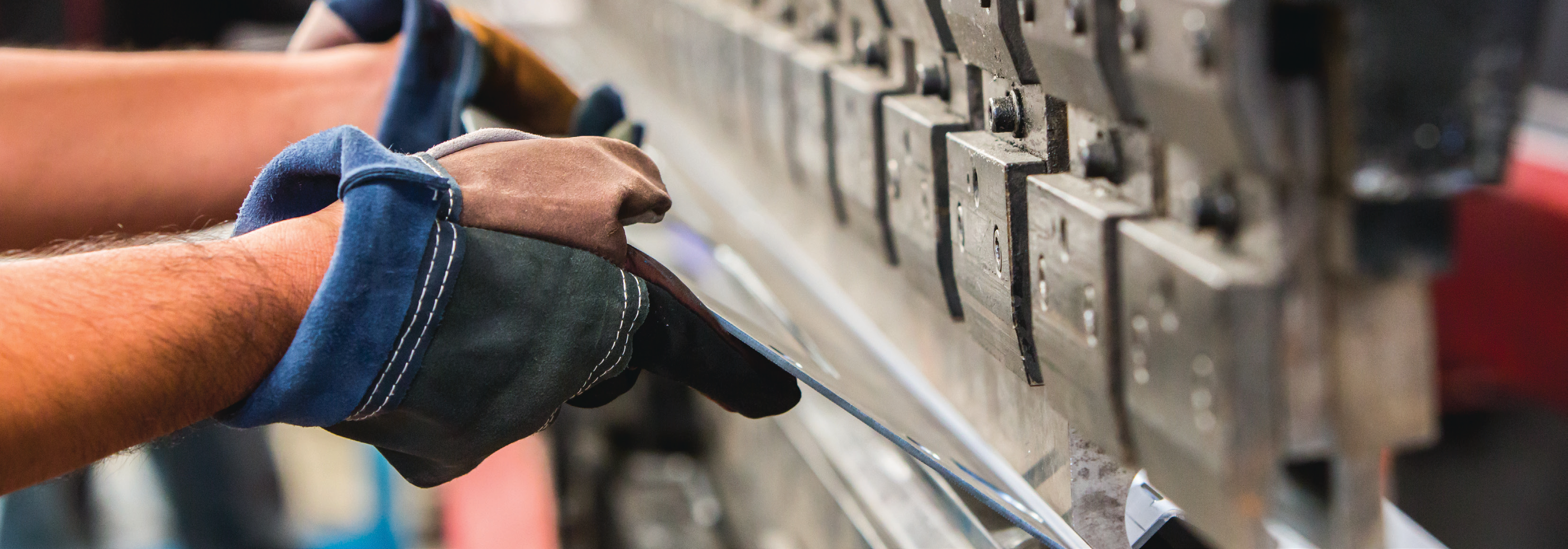 Worker wearing gloves operating a metal bending machine in a manufacturing facility