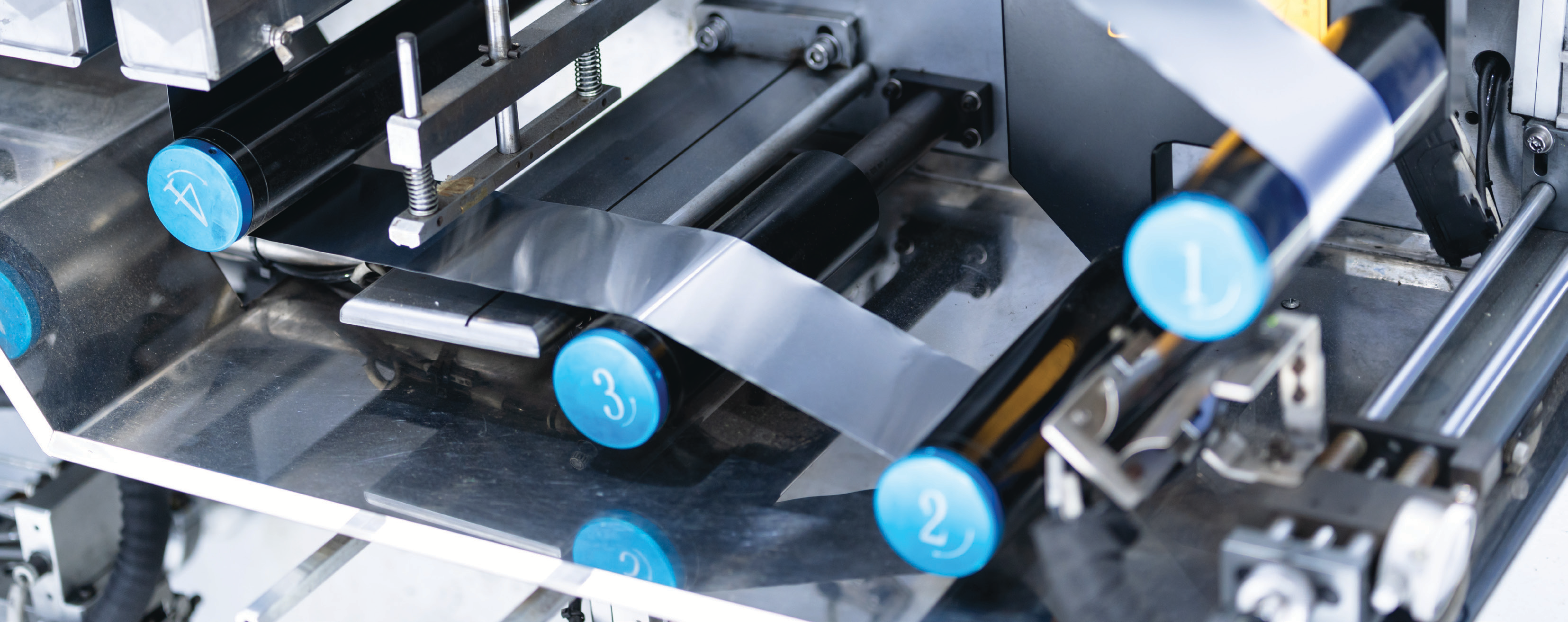 manufacturing equipment close-up photo with blue adjustment knobs and metal rollers