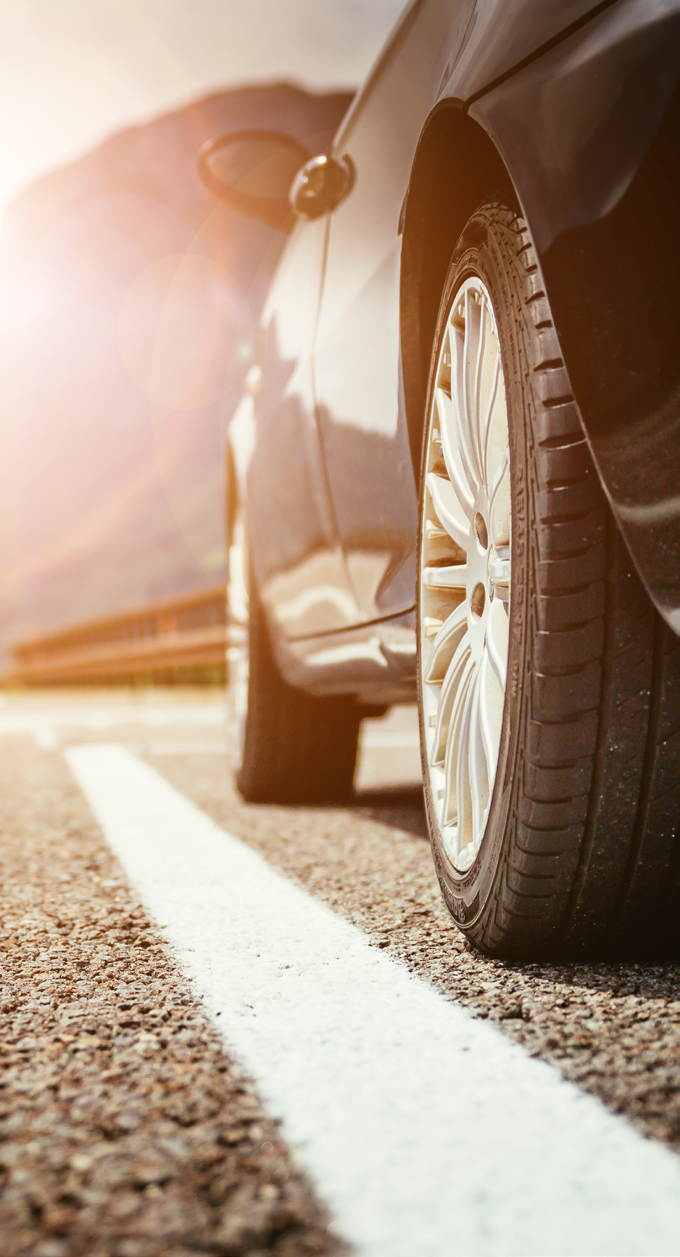 Close-up photo of a car tire on a sunlit road with a warm orange glow