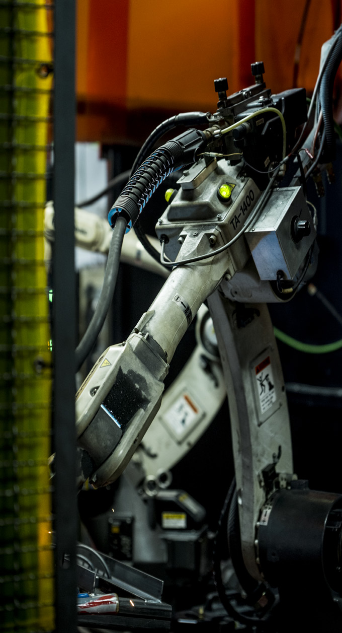 close-up photo of a robotic arm in a manufacturing facility with dark background and green lighting