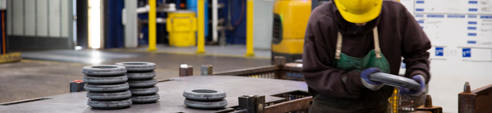 manufacturing facility interior photo with worker in yellow hard hat operating equipment