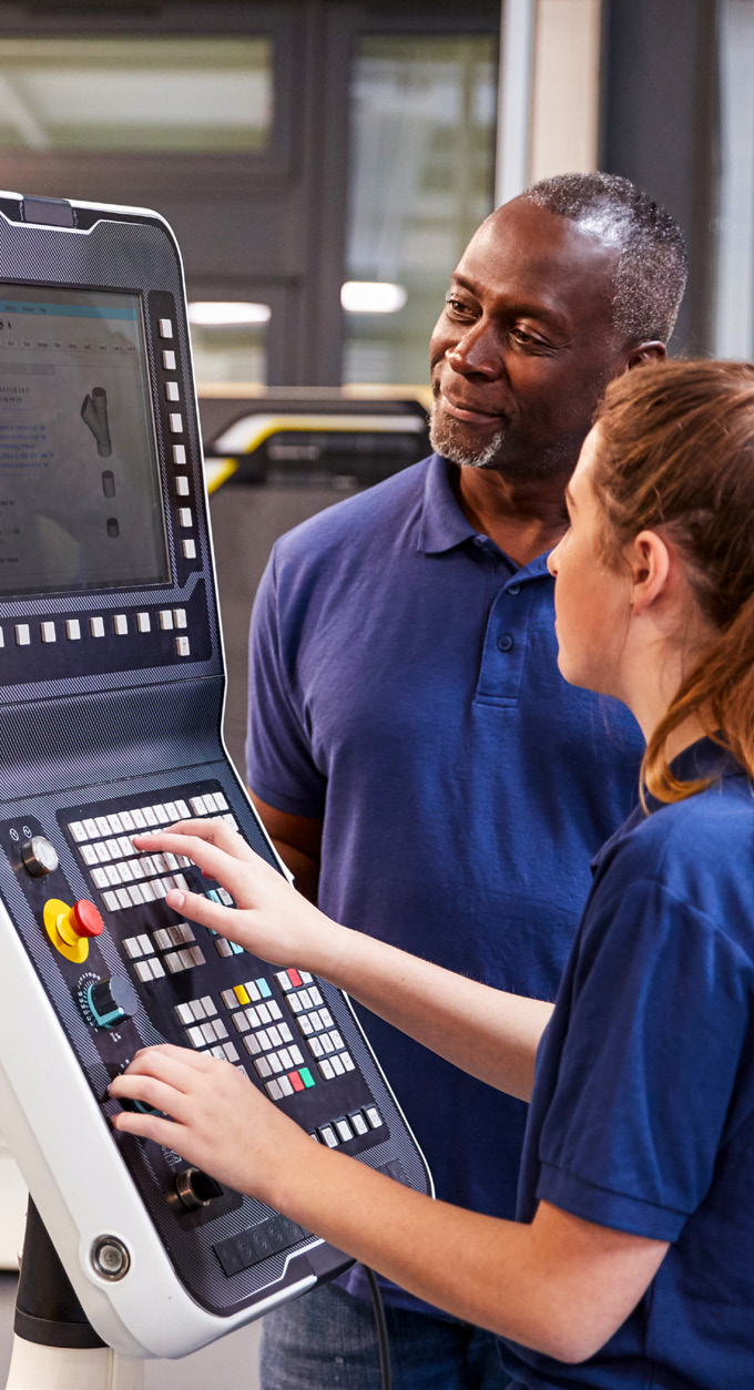 Two workers operating a large industrial control panel in a manufacturing facility