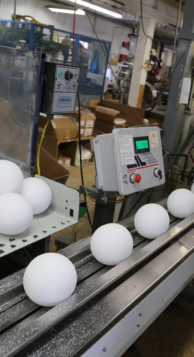 Manufacturing facility interior photo showing production line with white spherical objects on conveyor belt and control panels
