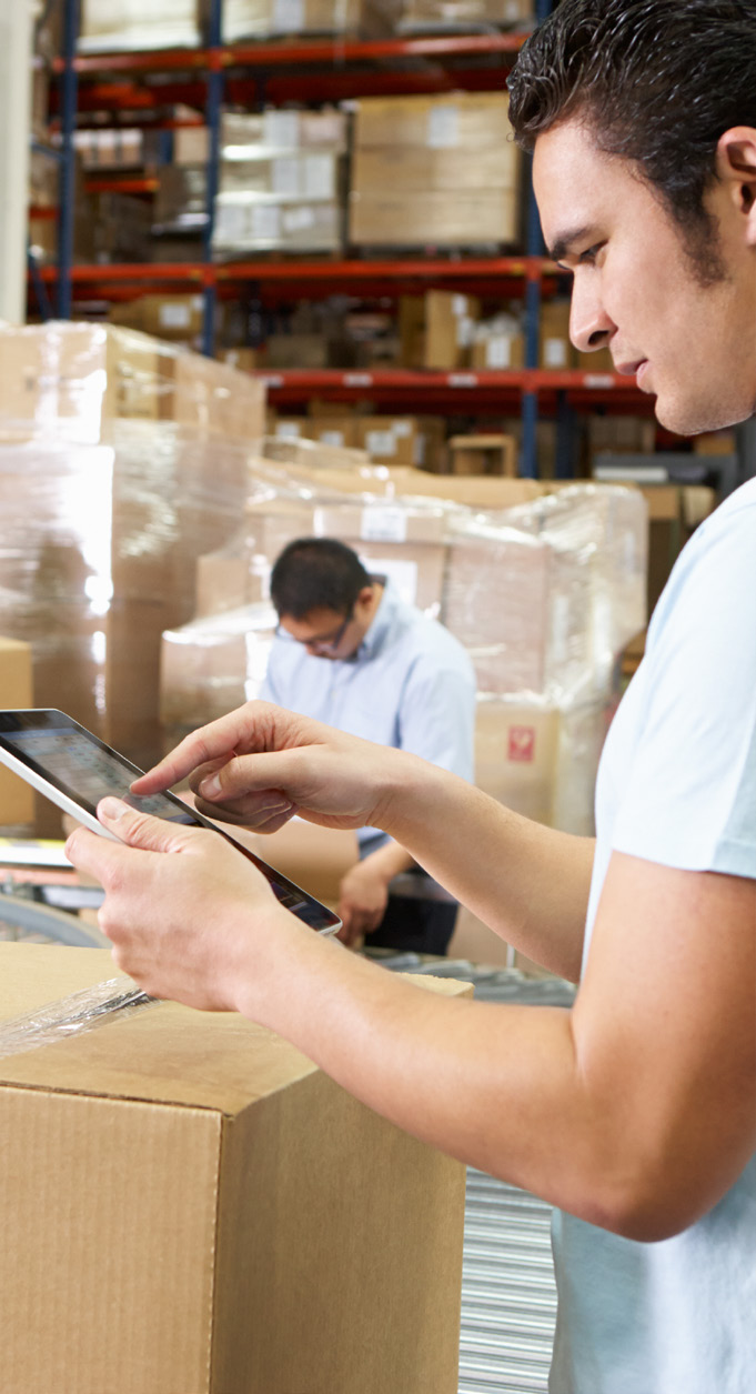 Warehouse worker using a tablet device in a storage facility with stacked boxes and inventory in the background
