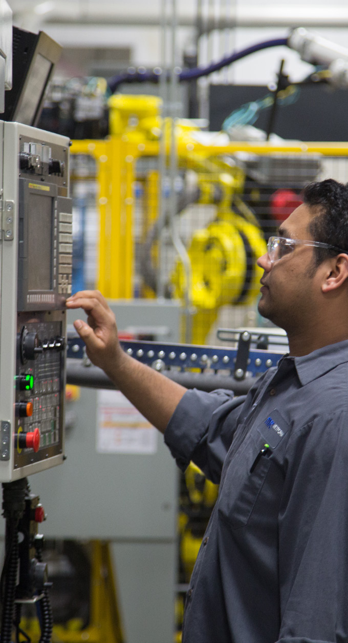 manufacturing facility interior with worker operating control panel and yellow robotic arms