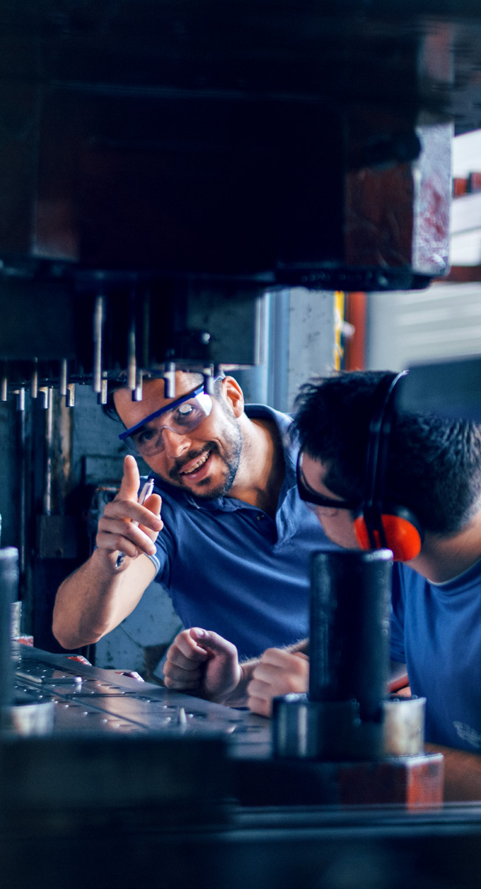 two men working on a mechanical device in a workshop with dark blue and red lighting