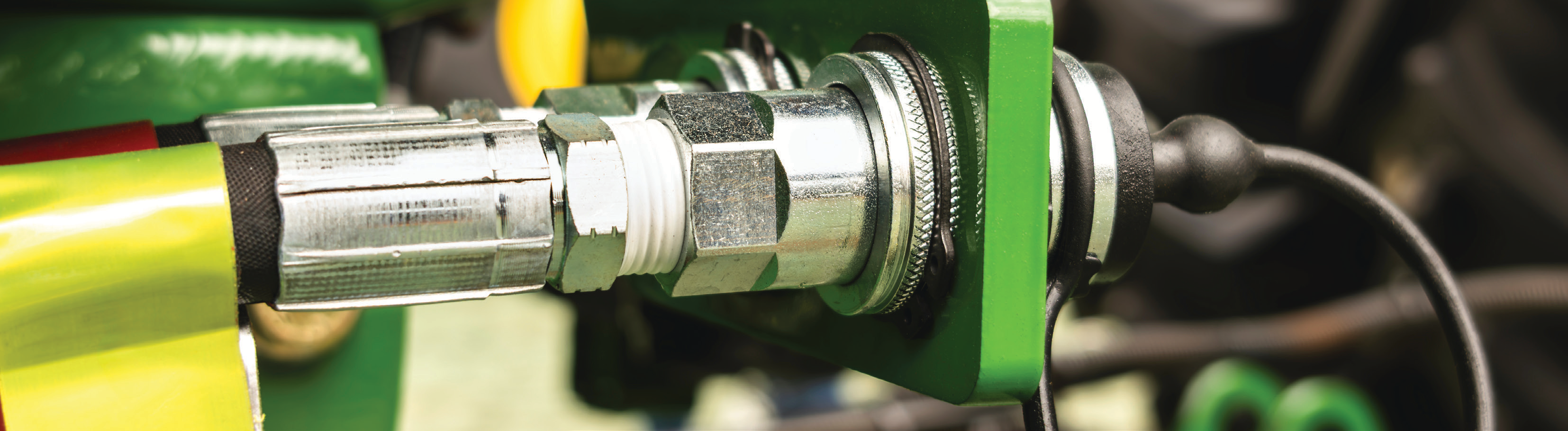 close-up photo of industrial metal pipe fitting with green and yellow cables in a manufacturing facility