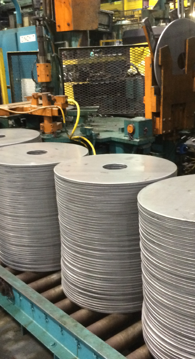 Manufacturing facility interior with large metal discs on conveyor rollers and industrial equipment