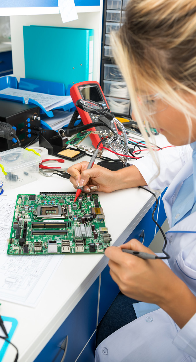 Technician working on a green circuit board with testing equipment in a laboratory environment