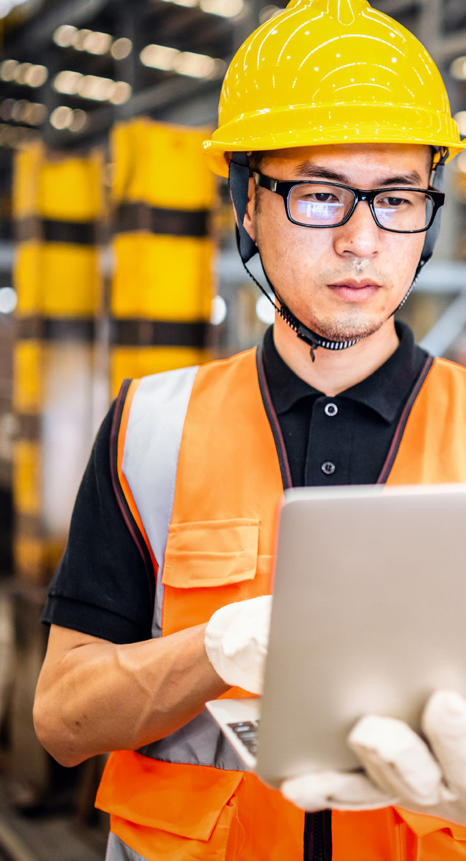 Worker in orange safety vest and yellow hard hat in a manufacturing facility