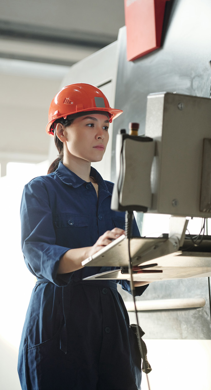 Manufacturing facility interior photo with worker in red helmet operating control panel