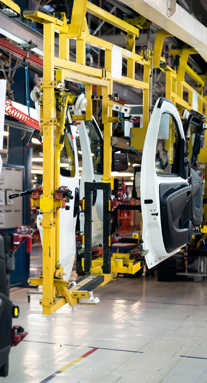 Manufacturing facility interior with vehicle assembly line and yellow overhead cranes