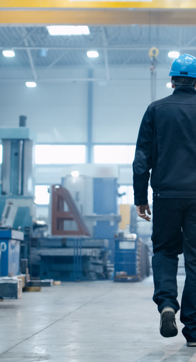 manufacturing facility interior with worker walking away from camera wearing blue helmet
