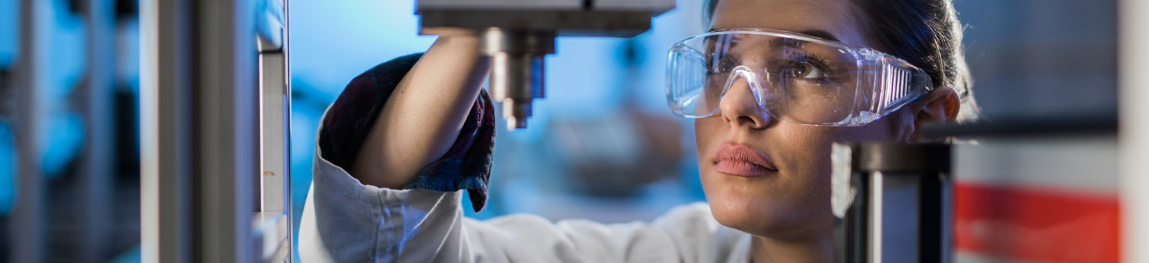 woman wearing safety glasses working on a machine in a manufacturing facility