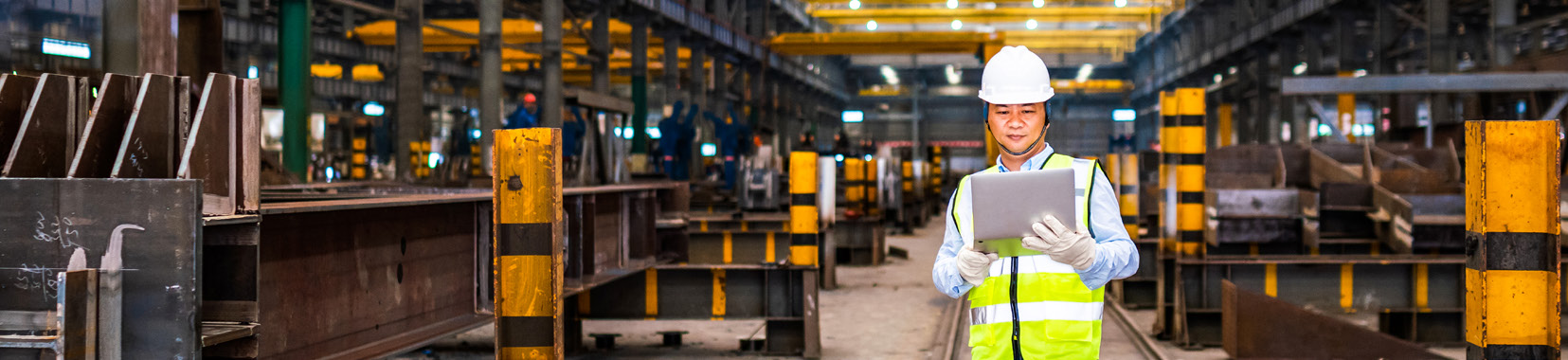 manufacturing facility interior with worker in high-visibility vest holding a tablet