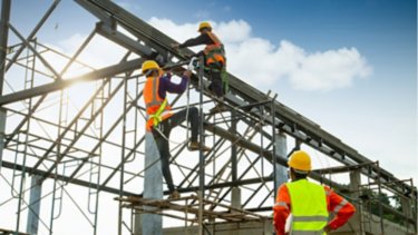 Two construction workers in neon vests working on outdoor construction site wiring structure