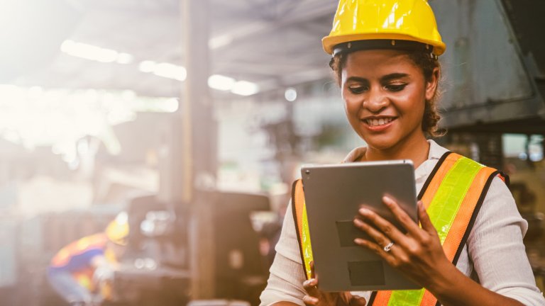 Female engineer holding a tablet on a modern factory plant floor. Analyzing critical cyber alerts via Rockwell Automation Security Monitoring and Response.