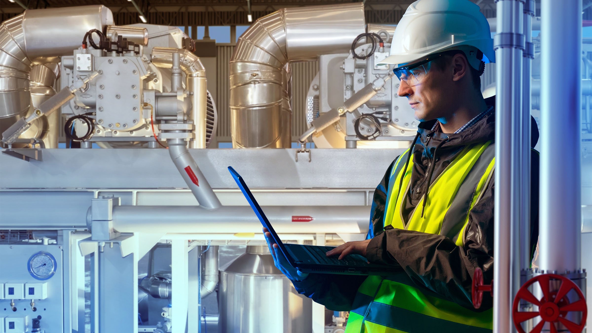 Production engineer with laptop near equipment in a chemical manufacturing plant.