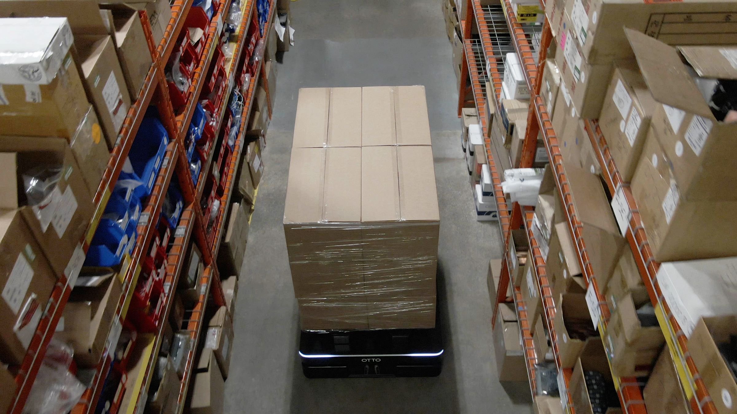 An overhead view of an OTTO 1200 AMR operating in a narrow aisle with pallet racking full of boxes on either side of it.