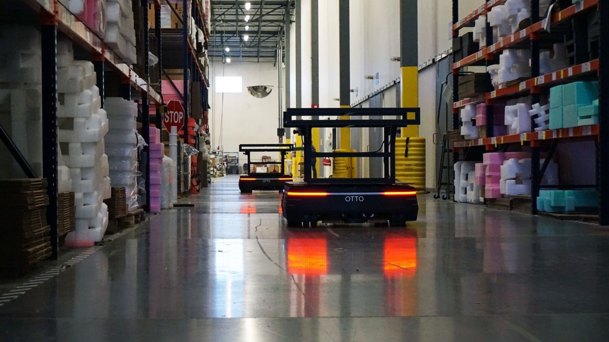 Two OTTO 1500 AMRs moving down an aisle in a life sciences warehouse with pallet racking on either side.