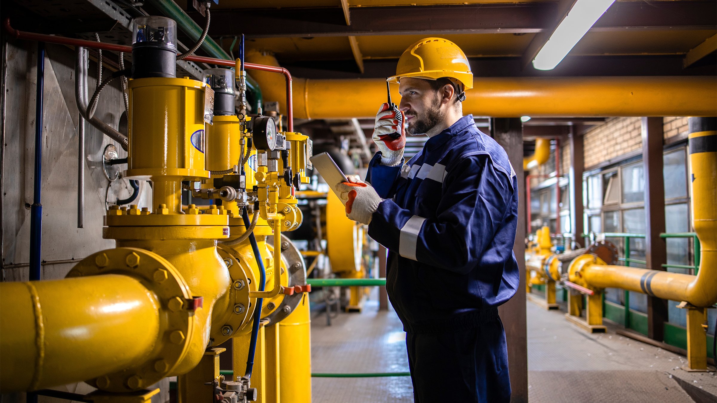 Professional caucasian refinery worker in safety equipment checking gas pipeline installation and pressure.