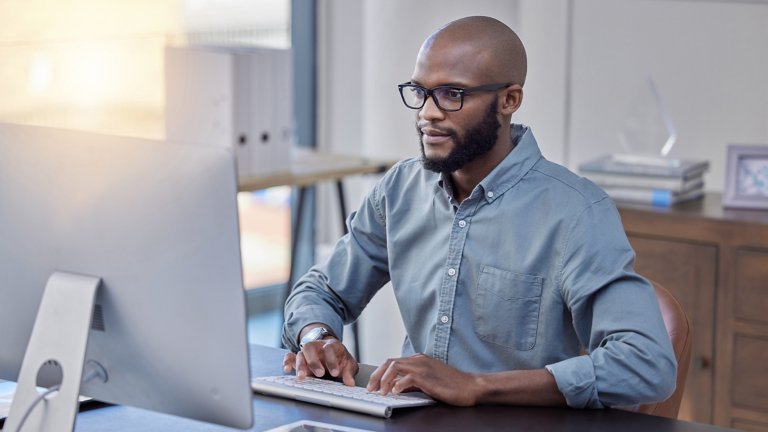 A man sits at a desk typing on a keyboard and looking at a computer in an office