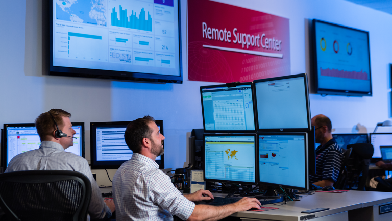 Dos hombres miran pantallas de computadora en una sala de control de un centro de asistencia técnica remota