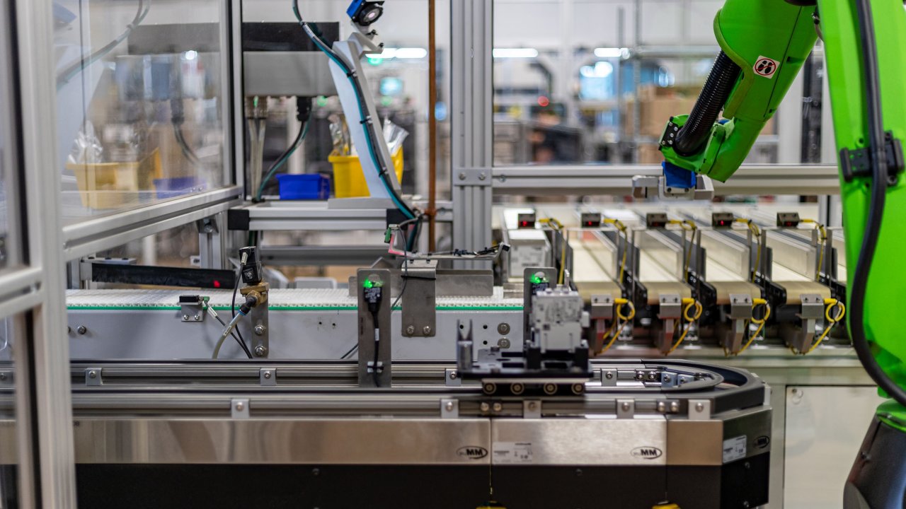 A green FANUC collaborative robot placing a box while a contactor moves past on a MagneMover LITE Intelligent Conveyor System carrier. 0222_000947_MKEContactorLine_Photography-658
