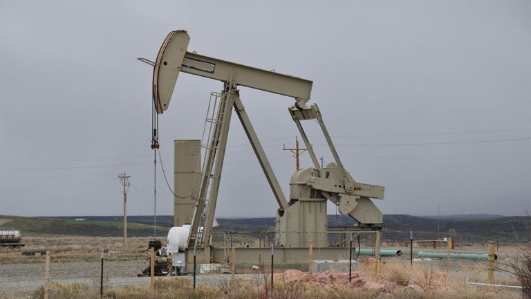 An old oil and gas pump operating in a grassy field with gray sky background.