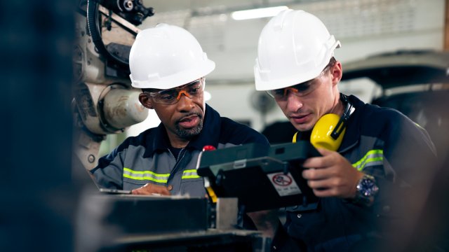 Two male engineers in a factory wearing white hardhats and looking at human machine interface monitor from containerized software