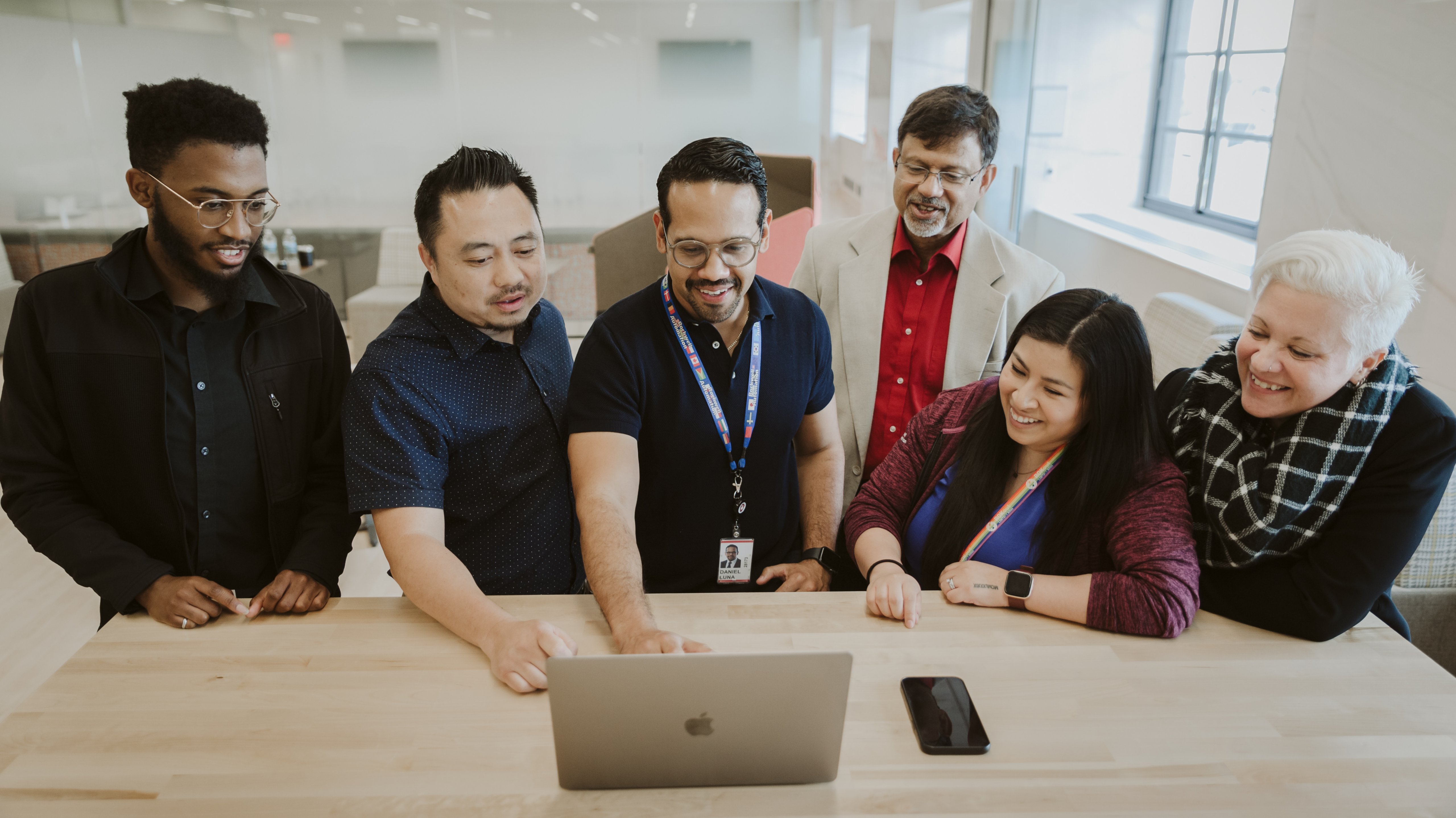 A group of employees in the office smiling looking at a laptop together
